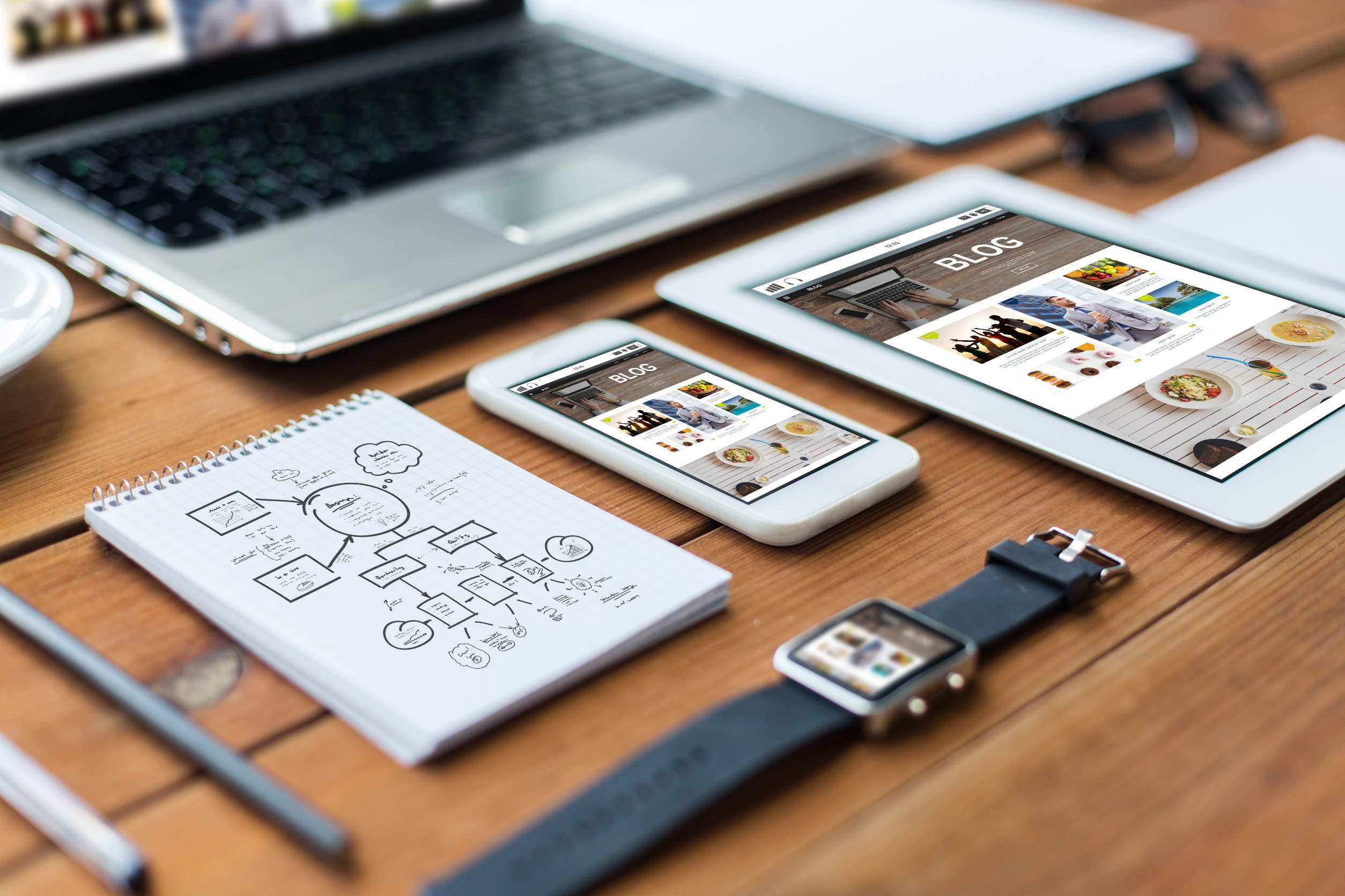 laptop, tablet, phone, watch and pad of paper on a table